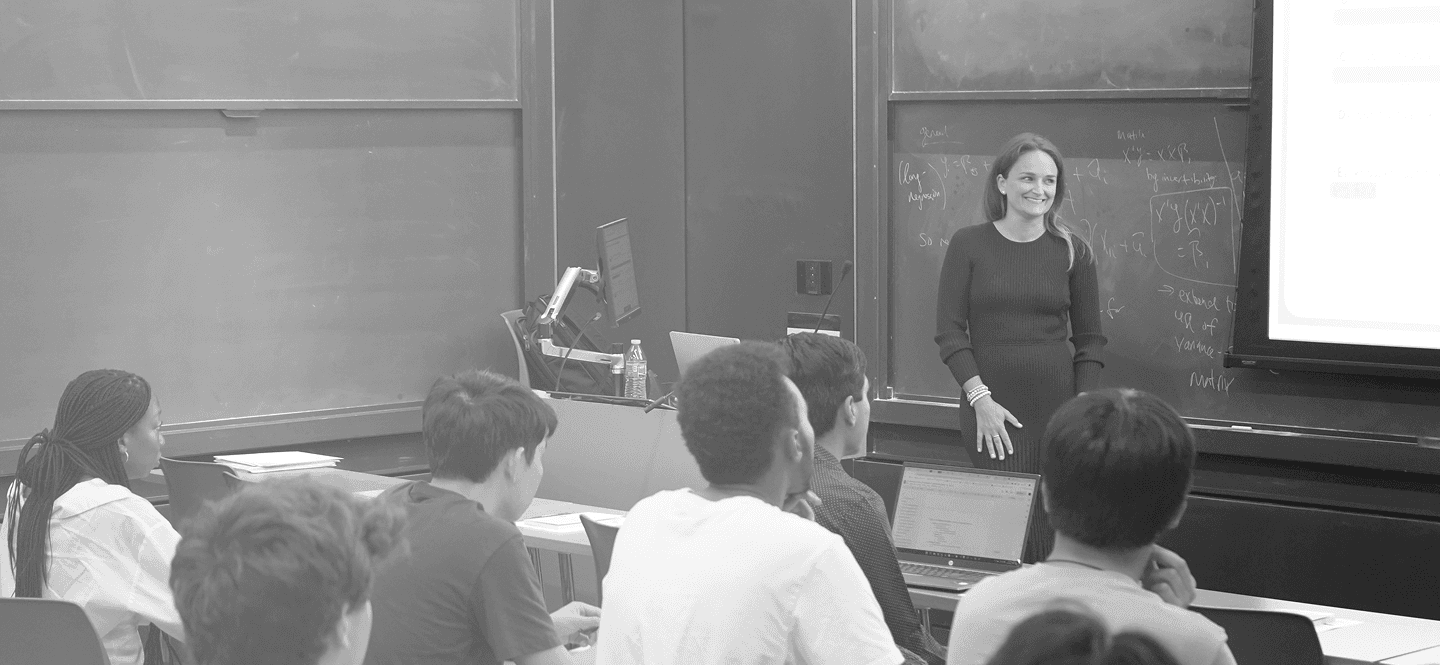 A woman smiling while presenting next to a screen in a classroom