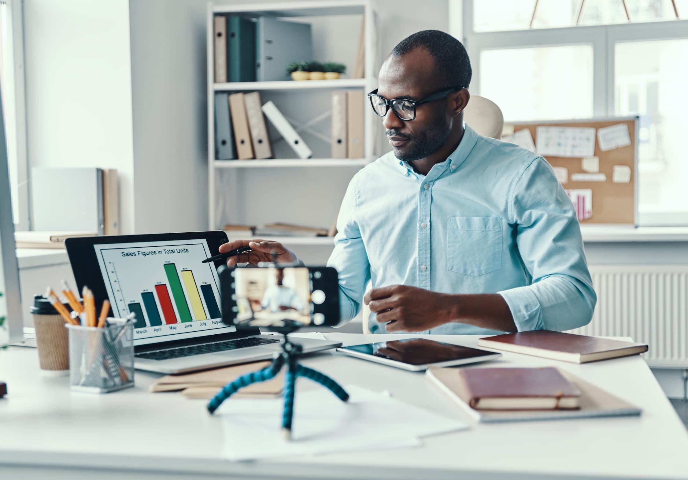 Intelligent young African man in shirt showing chart and telling something while making social media video